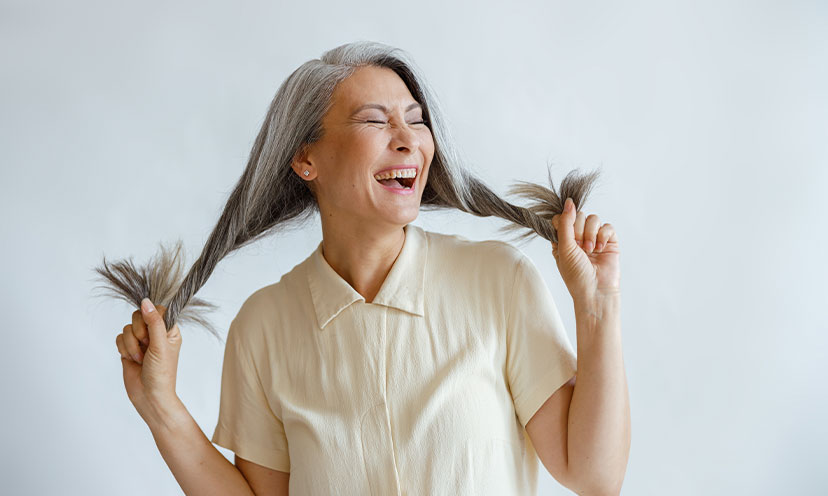 Woman with long gray hair hold it out to the sides and smiling big