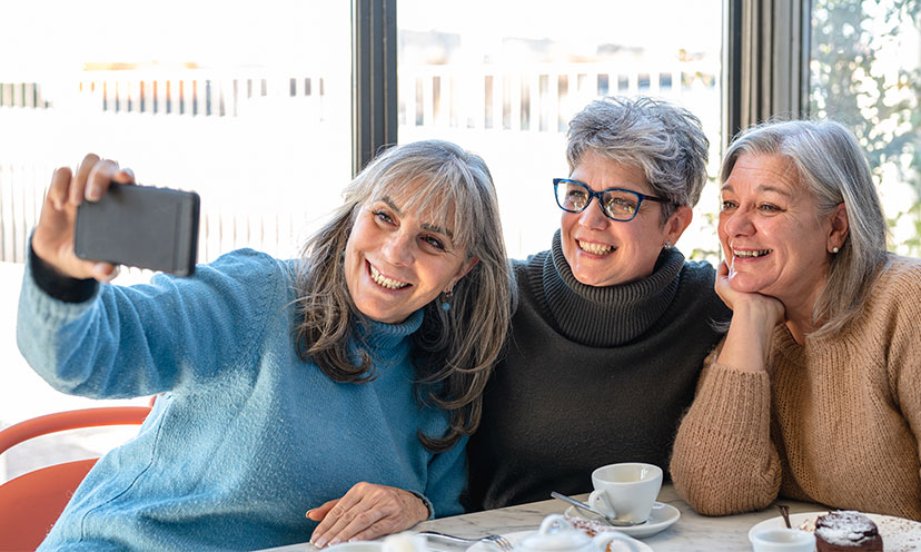 Women with gray hair take selfie around a restaurant table
