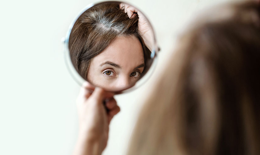 Woman looking in mirror at gray roots of hair